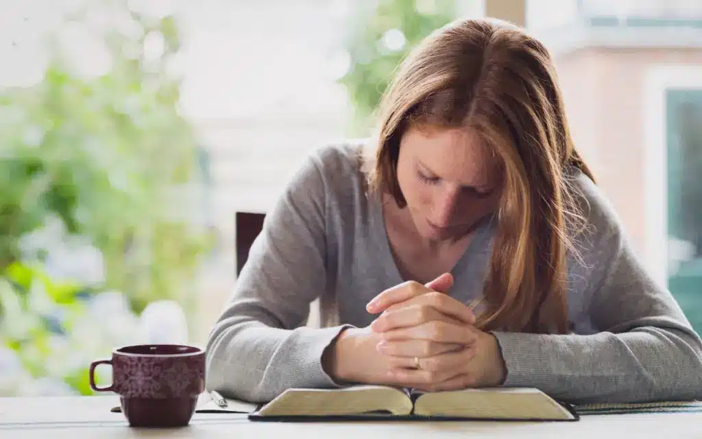 Uma mulher em oração, com as mãos delicadamente colocadas sobre uma Bíblia aberta.